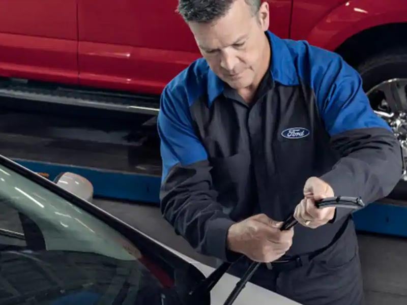 Mechanic replacing a windshield wiper blade on a car.